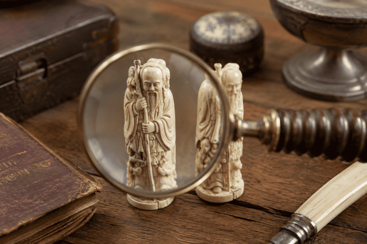 Magnifying glass examining antique ivory and bone carvings on a collector's desk, illustrating how to identify the difference between ivory and bone.