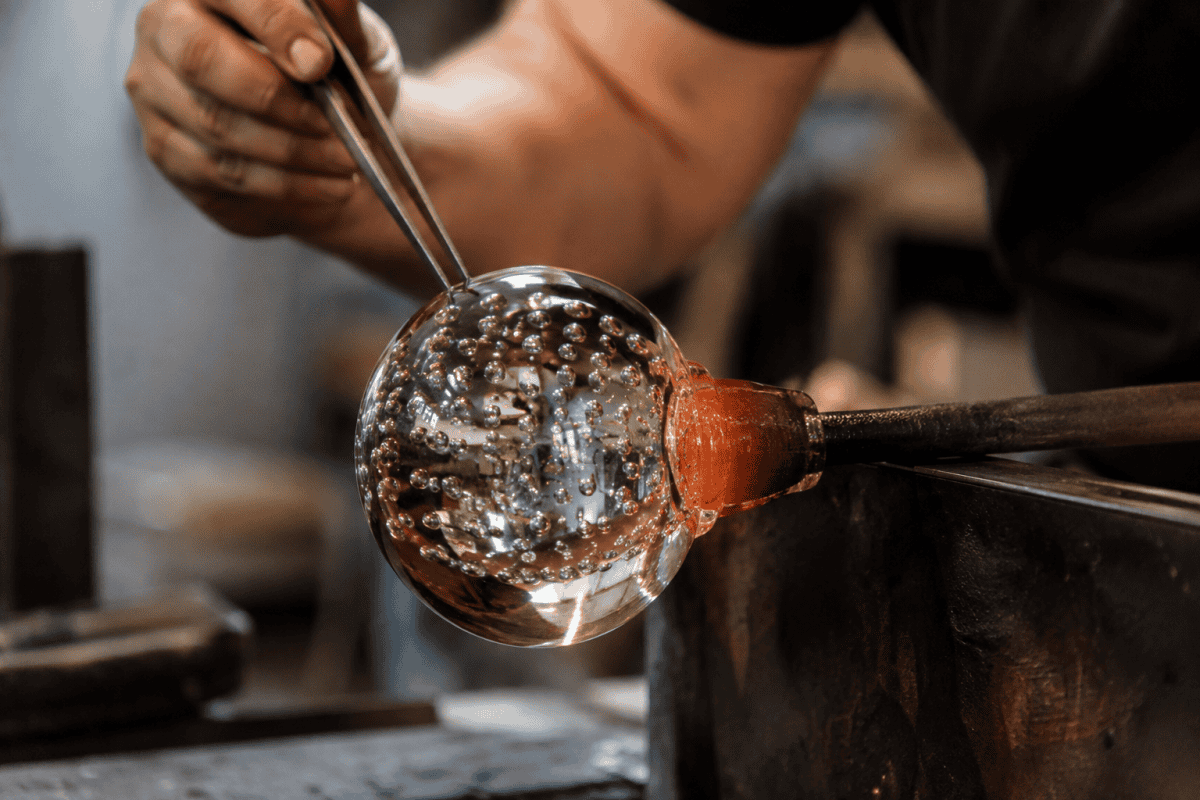 Glassmaker shaping a controlled bubble paperweight while molten glass remains on the blowpipe, showing the skilled craftsmanship behind deliberate bubble patterns.
